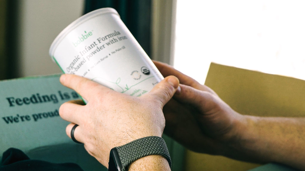 A pair of hands holding a can of Bobbie baby formula