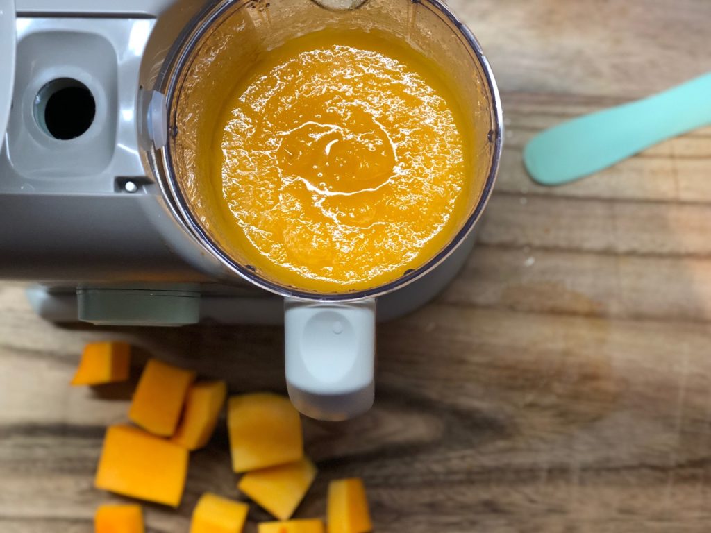 Looking down at some baby food made in a Beaba Babycook, placed on a counter next to butternut squash cubes