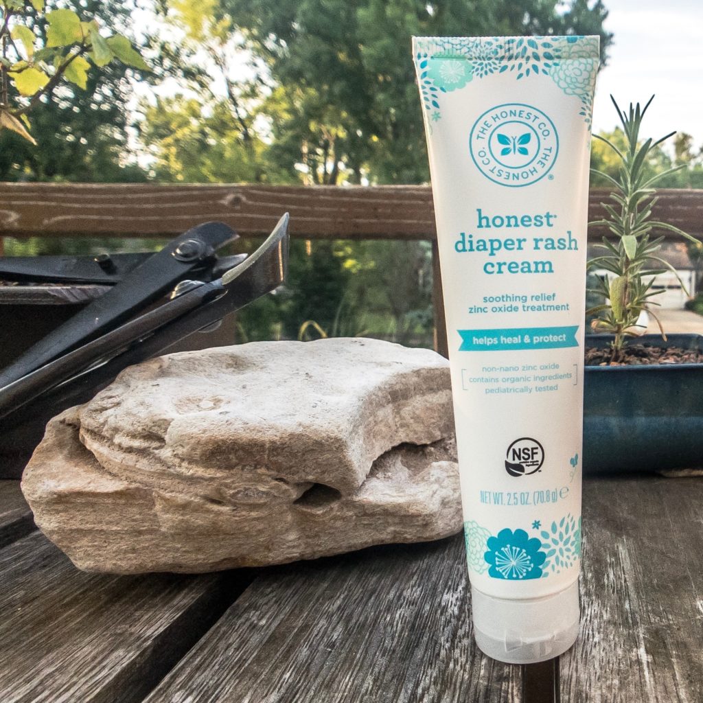 Honest Company diaper rash cream on a wooden table with a rock next to it outside