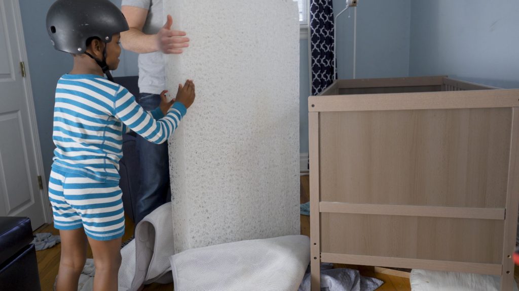 A boy in pajamas with a bicycle helmet holding the Newton crib mattress