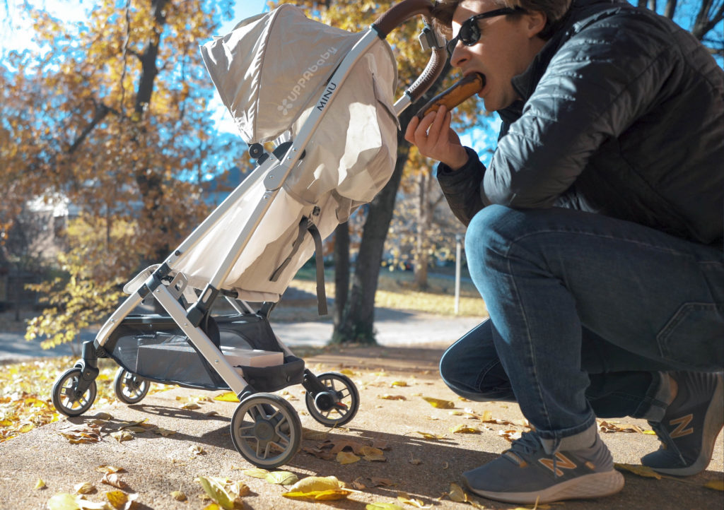 Guy eating a donut in front of an Uppababy Minu at the park